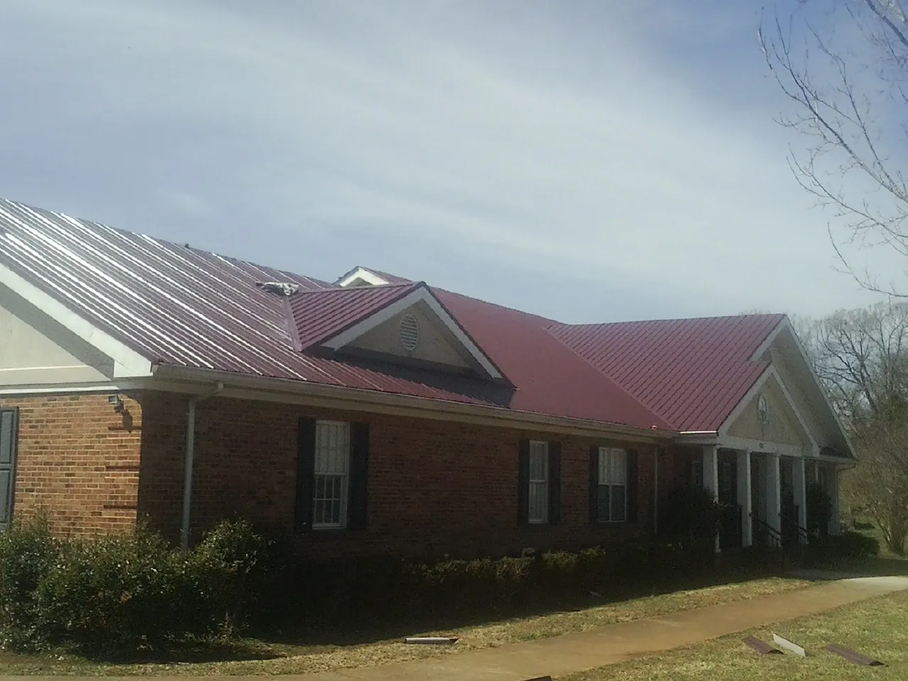 Red metal roof with gabled entries on a long brick building, from a Hail Damage Roof Repair job in Waltersburg