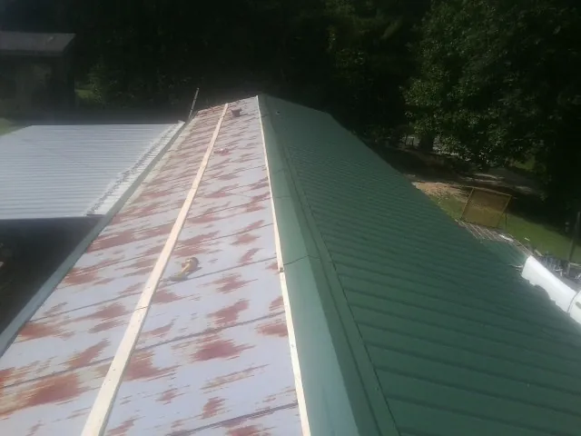 Old rusted panels beside newly installed green metal roofing — Wind Damage Roof Repair by Roofing Brothers in Waltersburg