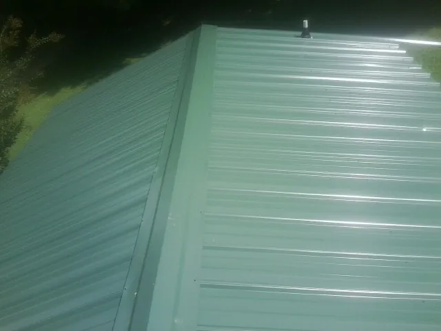 New green metal panels meeting at the ridge of a roof — Flat Roof Repair work by our crew in Waltersburg