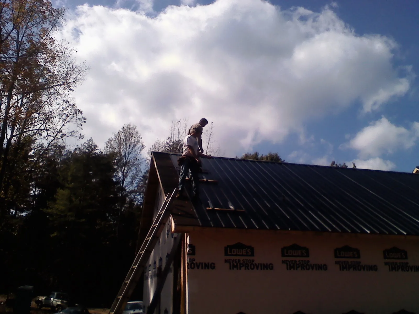 Roofer fastening dark metal panels high against a cloudy sky, from a Roof Inspection job in Waltersburg