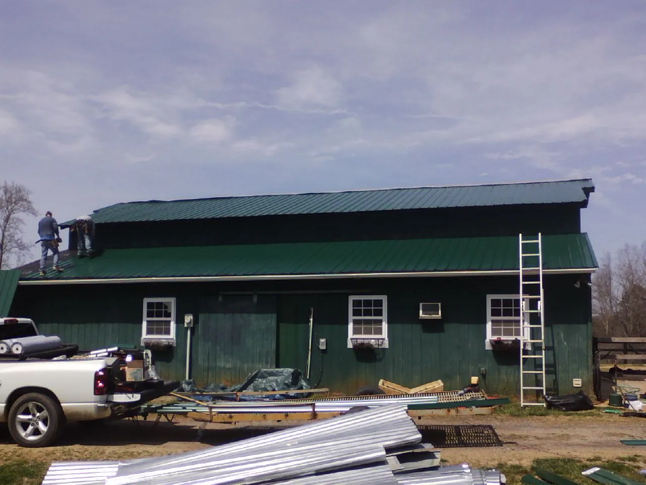 Crew installing green metal roofing on a large green barn in Waltersburg