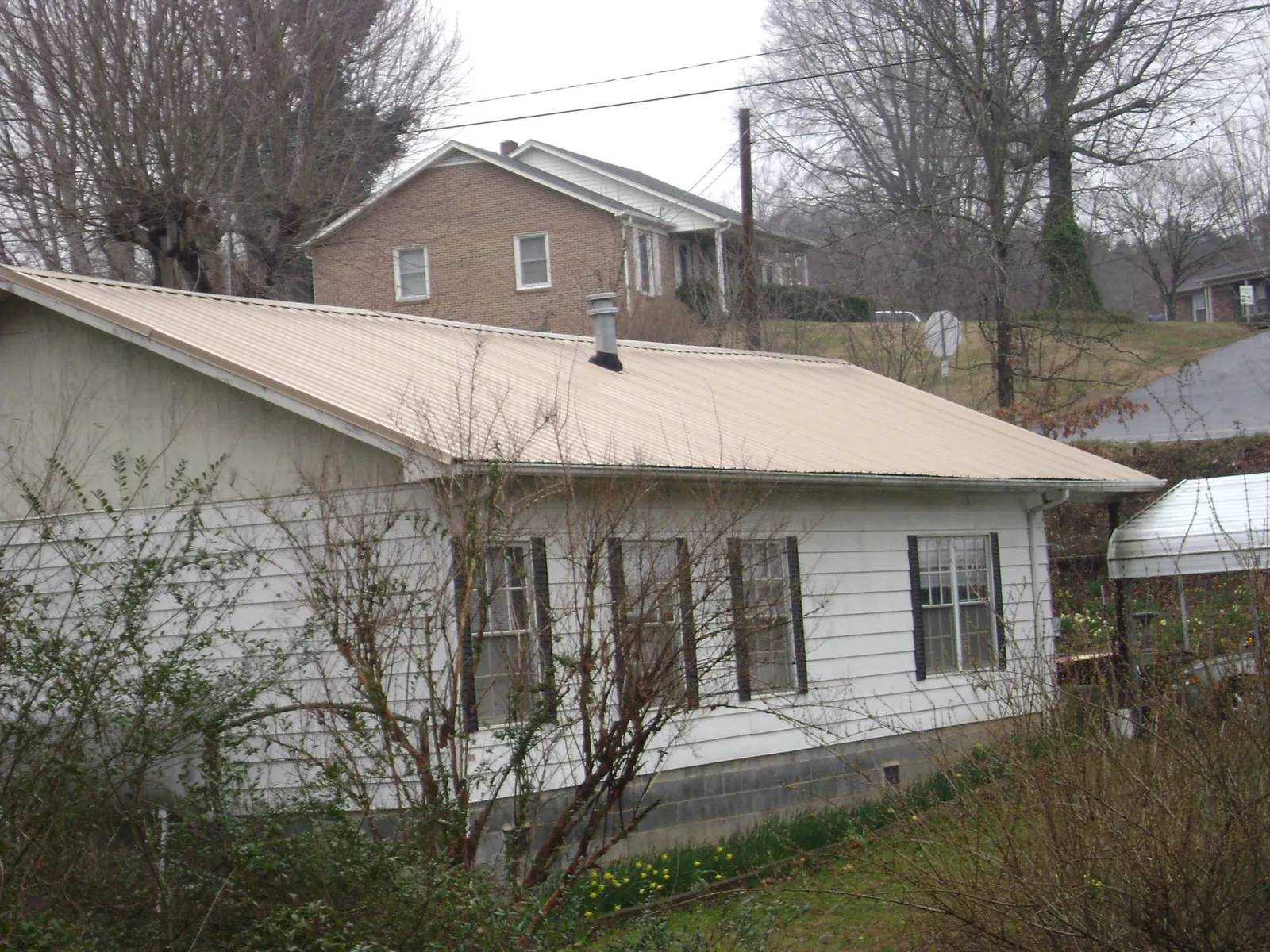 Tan metal roof on a white sided house set into a hillside — Commercial Roofing by Roofing Brothers in Waltersburg